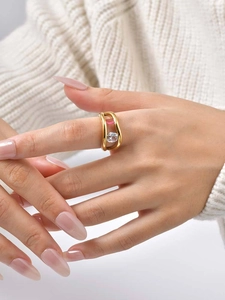 Close-up of wavy gold ring featuring pink rectangular gemstone and white round zircon
