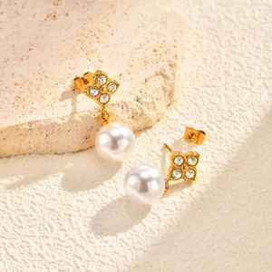 Détail macro de boucles d'oreilles trèfle en or avec strass et perles blanches