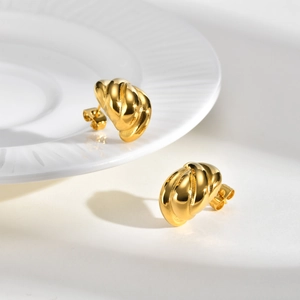 Golden teardrop twisted hoop earrings in minimalist style on white ceramic background