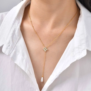 Vue détaillée d'un collier trèfle doré avec perle en goutte sur une chemise blanche