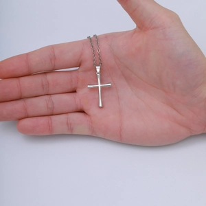 Detail of silver stainless steel cross pendant held in hand with delicate twist chain