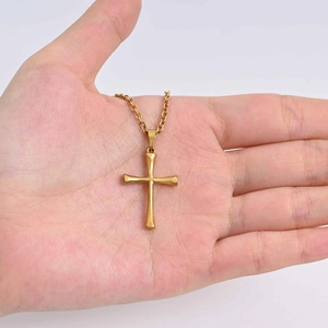 Detailed view of a gold cross pendant necklace held in hand to showcase its real size
