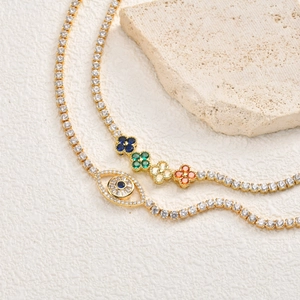 Gros plan de chaînes tennis dorées avec pendentif œil et trèfles colorés