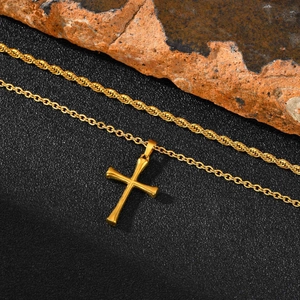 Polished gold stainless steel cross pendant on twisted rope chain against dark rock