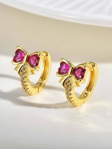 Macro detail of gold-plated hoop earrings featuring a zircon bow and pink heart stones