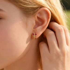 Close-up of a model wearing a gold bow earring with pink gemstones and white zircons