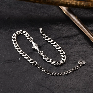 Close-up of silver stainless steel curb chain bracelet with a star charm on black stone