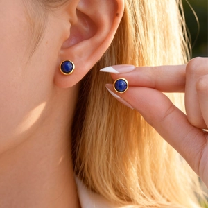 Detailed close-up of golden stainless steel stud earrings with lapis lazuli stones on ear