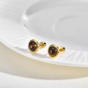 Detailed shot of golden stainless steel stud earrings with tiger eye stone on white porcelain