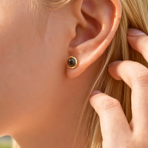 Macro shot of gold stud earring featuring a natural tiger eye stone on a model's ear