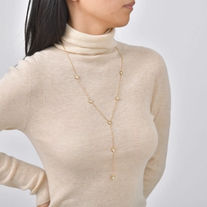 Dettaglio della collana lunga a Y dorata con ciondoli a cuore su maglione beige