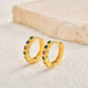 Detail of gold hoop earrings with multi-colored round zircon stones on stony texture