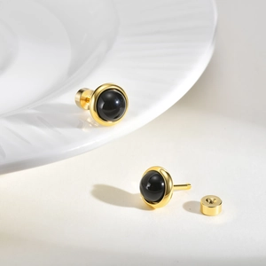 Detail of round black onyx stud earrings with gold screw backs on a ceramic plate