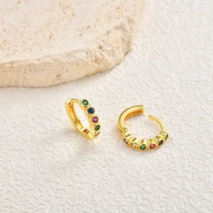 Detail of gold huggie earrings with vibrant multi-color zircon stones on stone background