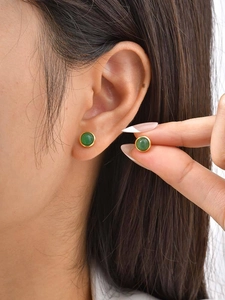 Detail view of round green gemstone stud earrings with gold bezel worn on earlobe