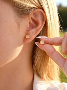 Close-up of elegant gold stud earrings featuring round pink moonstone on a model