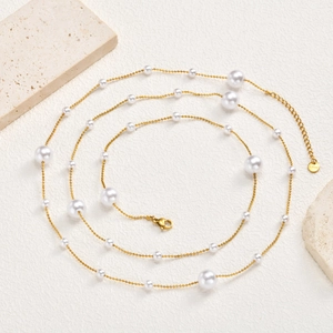 Dettaglio della collana a Y dorata a due strati con perle bianche e targhetta logo