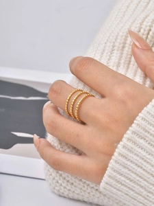 Close-up of triple layered gold bead rings worn with a white knit sweater