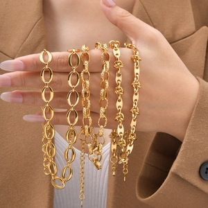 Set of six chunky gold-plated stainless steel link chains held by hand against a suit
