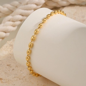 Macro shot of gold-plated rugby bead ankle bracelet on a white minimalist display stand