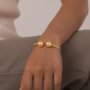 Bracciale rigido dorato aperto con due sfere lucide indossato da una modella