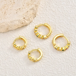 Golden huggie earrings with colorful zircon droplets on a minimalist stone background