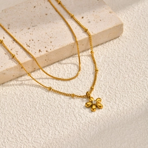 Double layered gold snake chain necklace with a floral pendant on a textured stone base