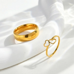Detail of minimalist gold double heart hollow ring and polished band on white pedestal