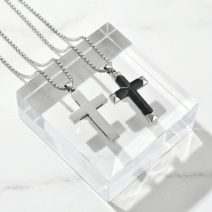 Polished stainless steel cross pendant necklaces with black onyx inlay on white marble surface