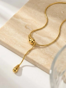 Vue détaillée du pendentif goutte d'eau dorée sur collier chaîne serpent et pierre