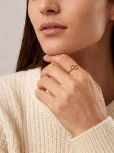 Close-up of a gold double heart ring worn on a finger with a cozy knit sweater background