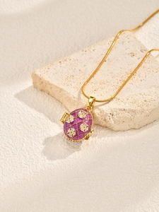 Macro view of purple enamel egg locket pendant with gold grid and white zircon floral detail