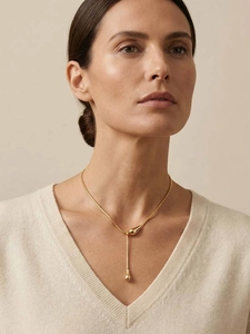 Gros plan détaillé d'un collier en Y doré avec gouttes d'eau sur un pull beige