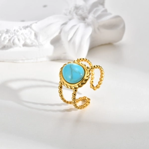 Detail shot of a double-layered gold ring featuring a round turquoise stone on white marble