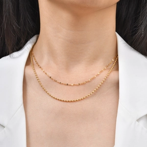 Close-up of golden layered double chain necklace on model with white blazer