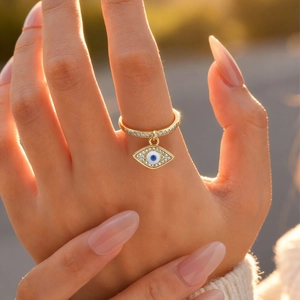 Close-up of a gold ring with a micro-paved zircon evil eye pendant worn on a finger