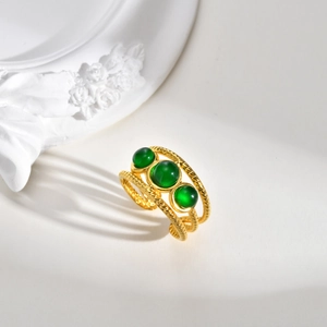 Détail d'une bague dorée torsadée avec trois pierres vertes sur socle en marbre