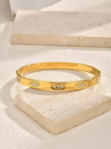Macro detail of gold zircon evil eye bangle on minimalist textured stone background