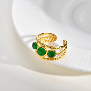 Bague ouverte en acier doré tressé avec trois pierres vertes sur une assiette en céramique
