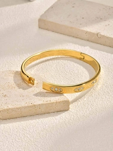 Detail of gold evil eye bangle with zircons and shell inlay on a natural stone base