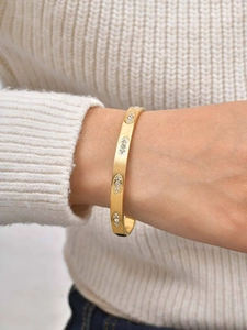 Detail of gold evil eye bangle with zircon on a white knit sweater background