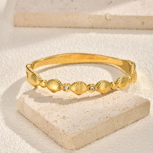 Detailed view of a gold shell-shaped bracelet with brilliant cubic zirconia and shell inlay