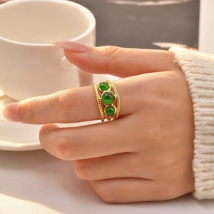 Détail d'une bague dorée torsadée à trois rangs sertie de trois pierres vertes au doigt