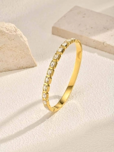 Detail of gold bracelet with rectangular zircon inlay on textured beige background