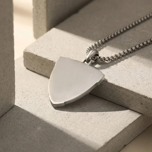 Macro detail of brushed stainless steel shield pendant on a box chain with stone background
