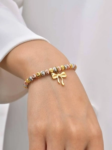 Detail of a tricolor beaded bracelet with golden bow pendant worn on a model's wrist