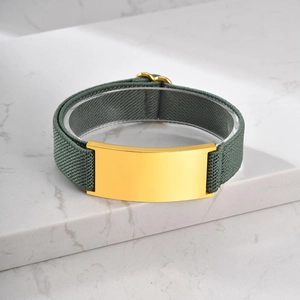 Detail view of dark green elastic fabric strap with polished gold metal plate on marble surface