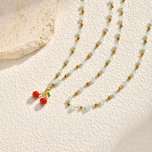 Macro detail of gold beads and blue cube beads with a red cherry pendant necklace
