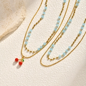 Double-layered gold cherry pendant necklace with light blue beads on textured white background