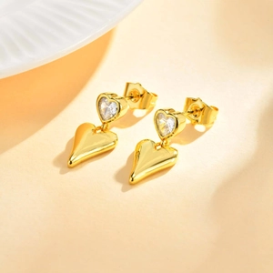 Golden heart drop earrings with zircon crystals on a warm minimalist background